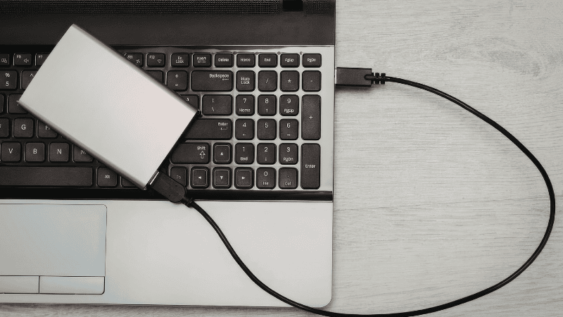 A high-end professional home office setup featuring a MacBook Air M5 connected to a 4K studio display via a single Thunderbolt cable, demonstrating a minimalist productivity workflow.