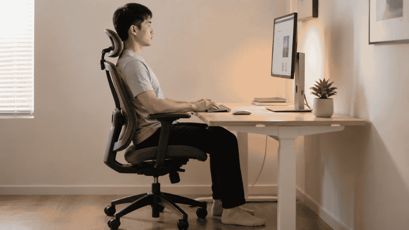 Person sitting in ergonomic office chair with correct posture — feet flat, back supported, arms at 90 degrees