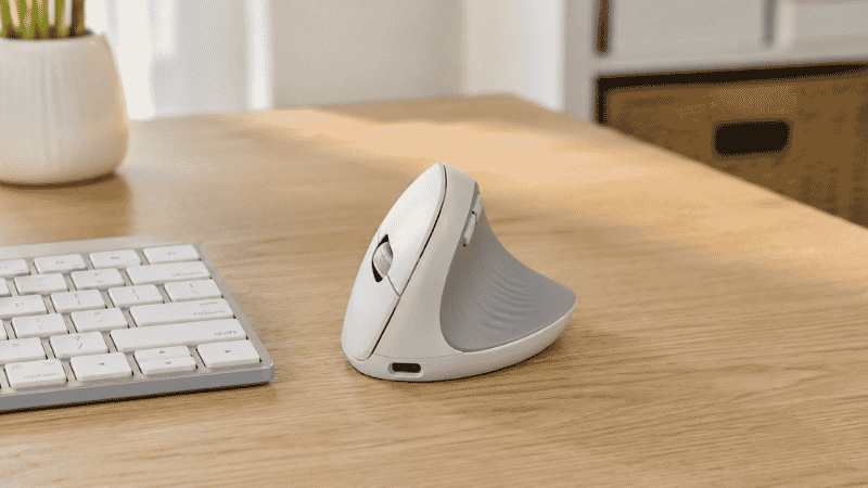 A vertical ergonomic mouse on a clean home office desk beside a keyboard showing the handshake grip position