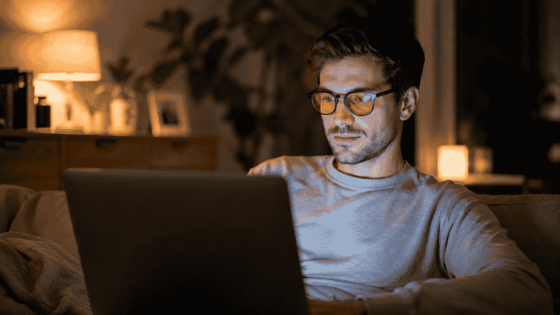 Person wearing blue light blocking glasses while using a laptop in the evening at home before bedtime