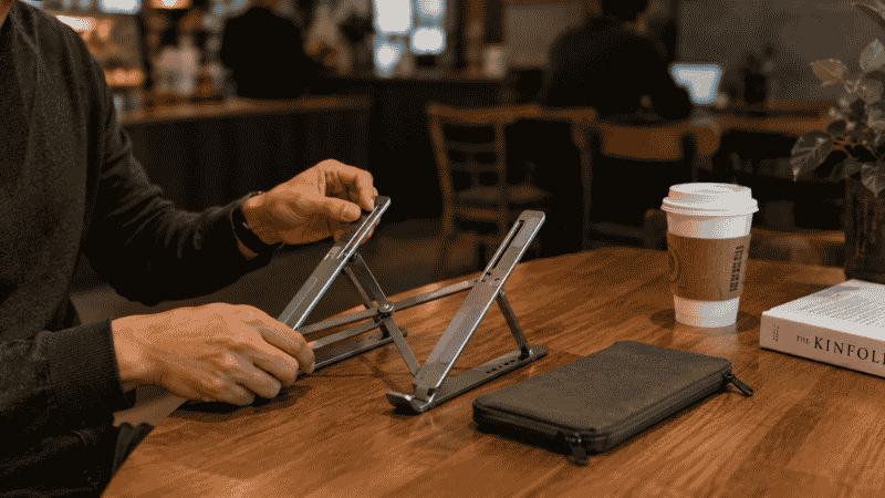 A compact foldable laptop stand being set up on a café table showing its portability for remote workers on the go
